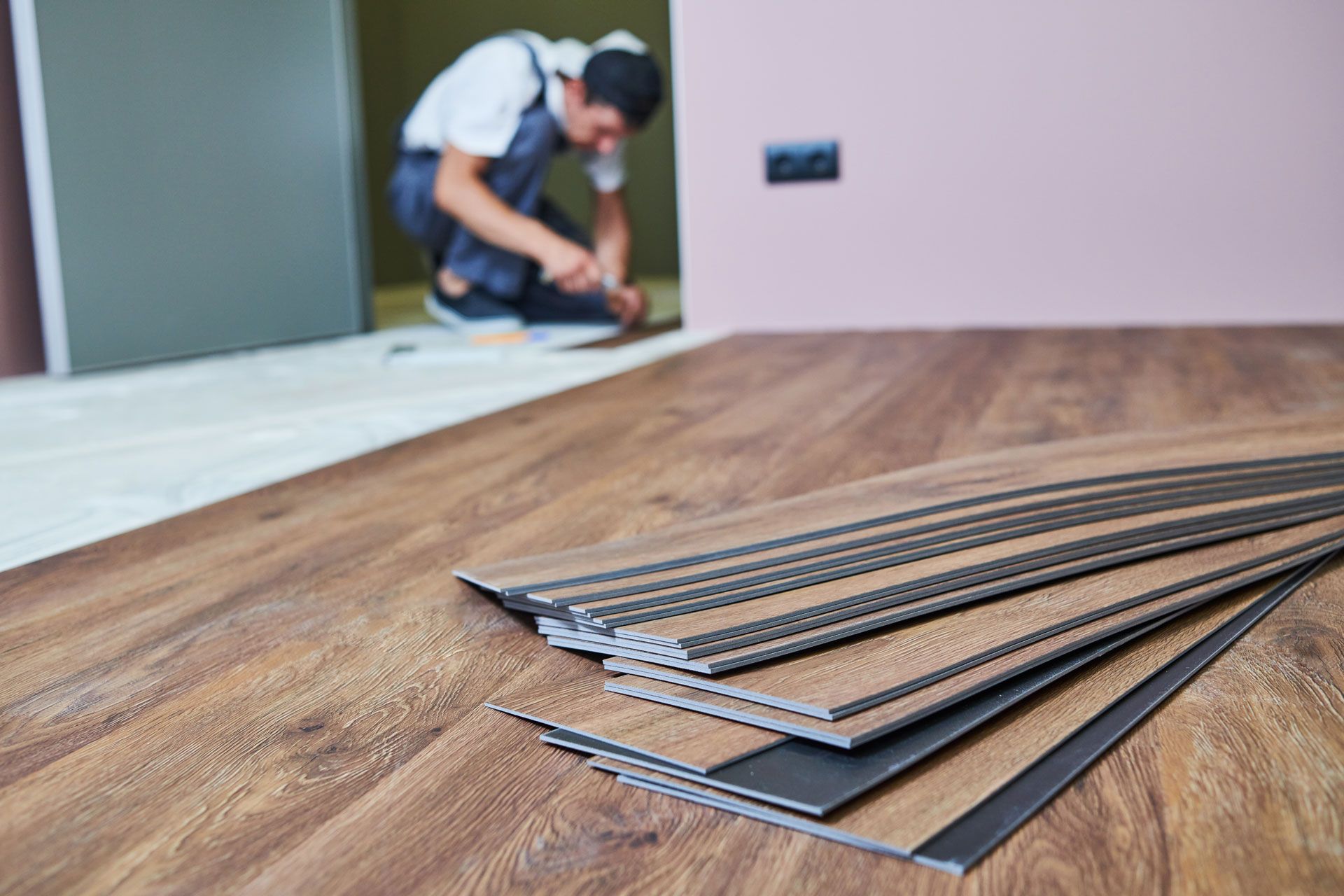 Wood flooring planks laid out in the foreground, with a worker installing flooring in the background.