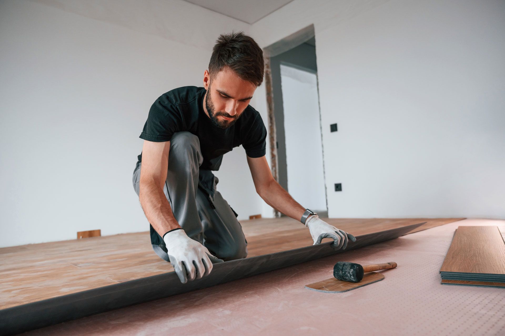 Worker installing flooring on a room floor with tools nearby