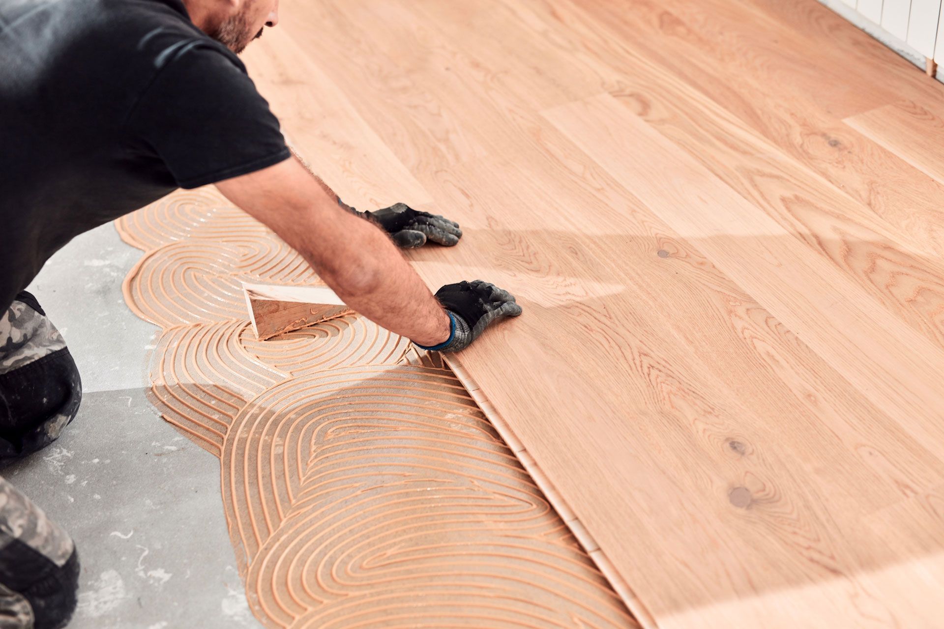 Worker spreading adhesive on a wood floor during installation