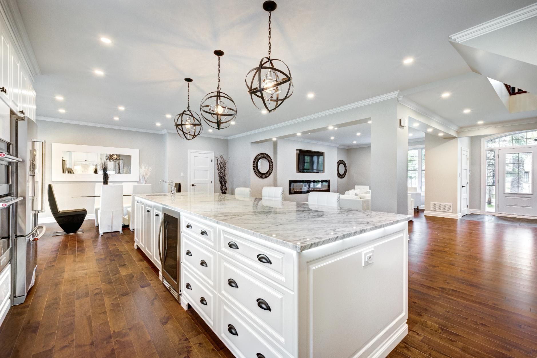Bright white kitchen with large island, pendant lights, hardwood floors, and open layout to adjacent living areas