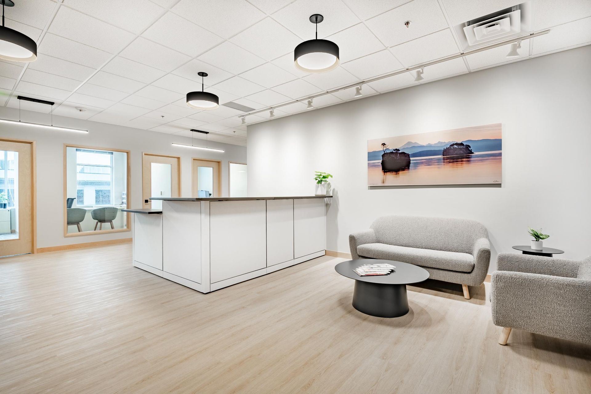 Bright modern office lobby with white reception desk, gray sofa, and landscape wall art