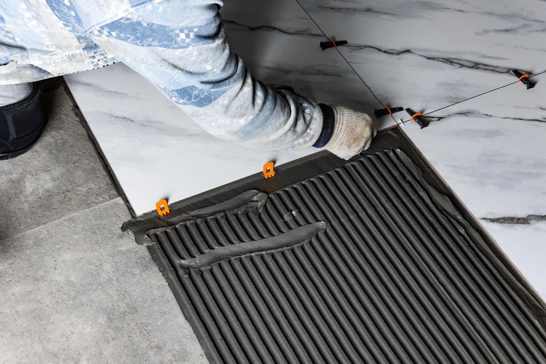 Person installing a black floor mat on a tiled floor, wearing a white protective suit and gloves.