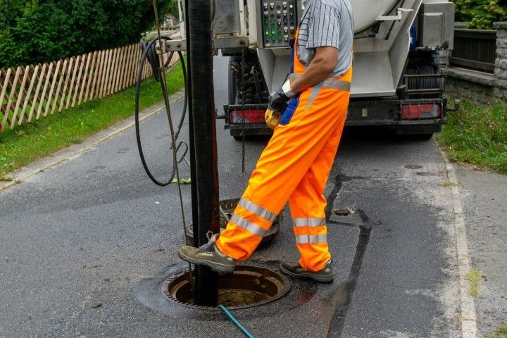 Worker in orange safety gear by a sewer, standing on the manhole cover. 
