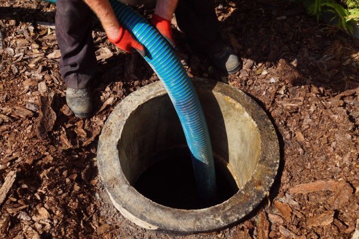 Person with red gloves using a blue hose to empty a round concrete well.