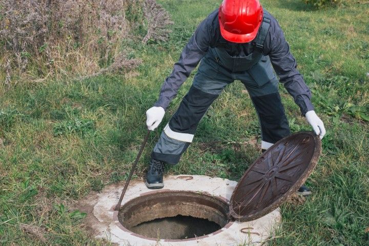 Person in safety gear opening a manhole cover in grassy area.