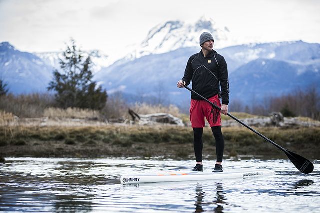 Person paddleboarding on calm water with snowy mountains in the background