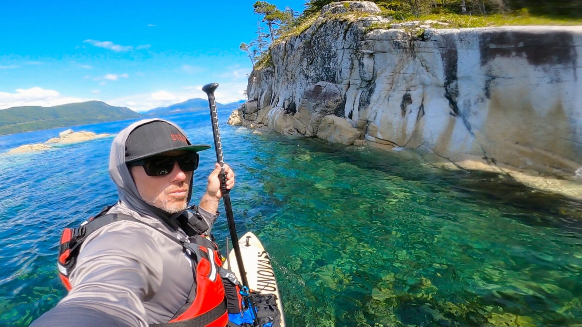 Person kayaking on clear turquoise water beside white cliffs under a sunny sky