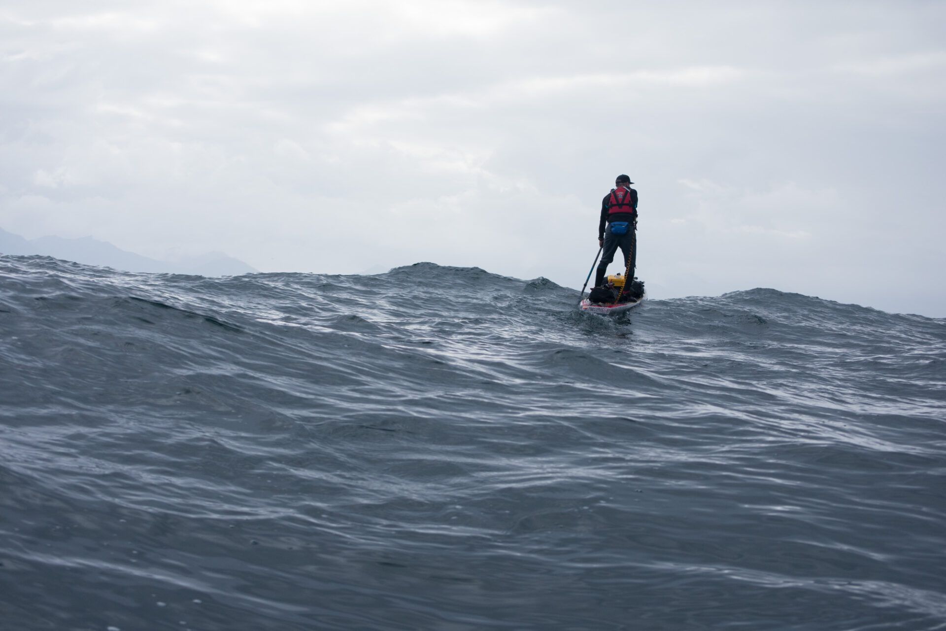 Person standing on a surfboard in rough ocean waves under a cloudy sky