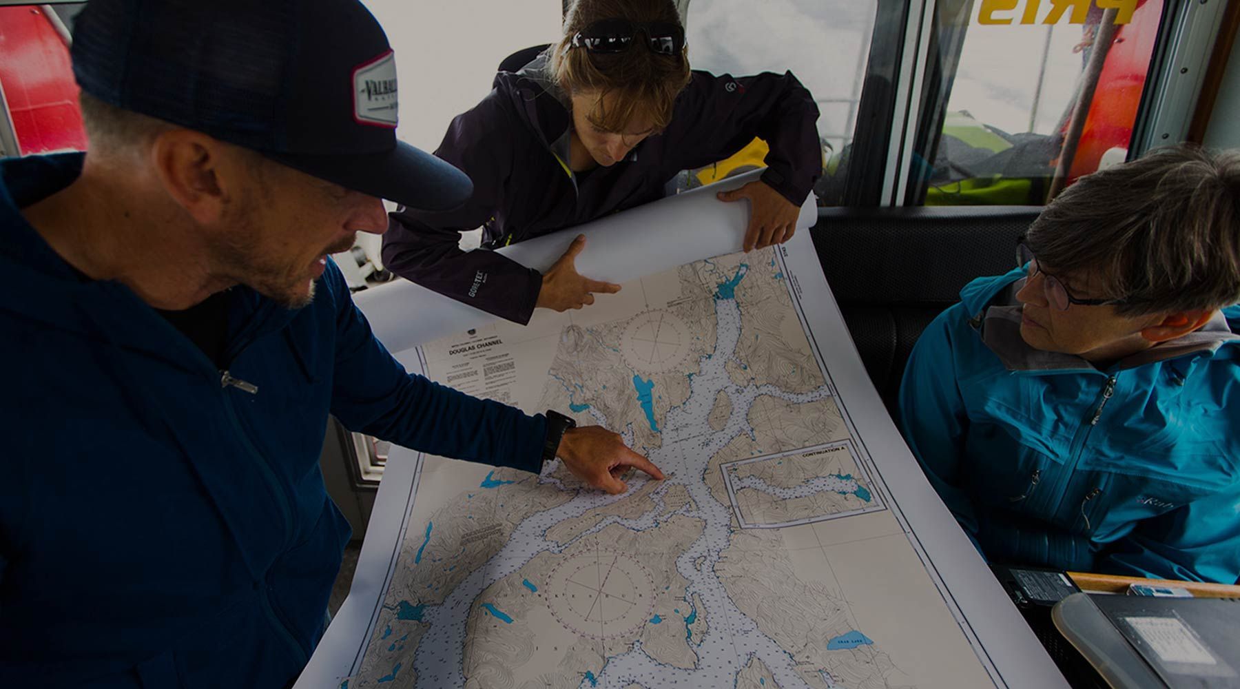 Three people study a large map inside a vehicle, pointing at routes and landmarks.