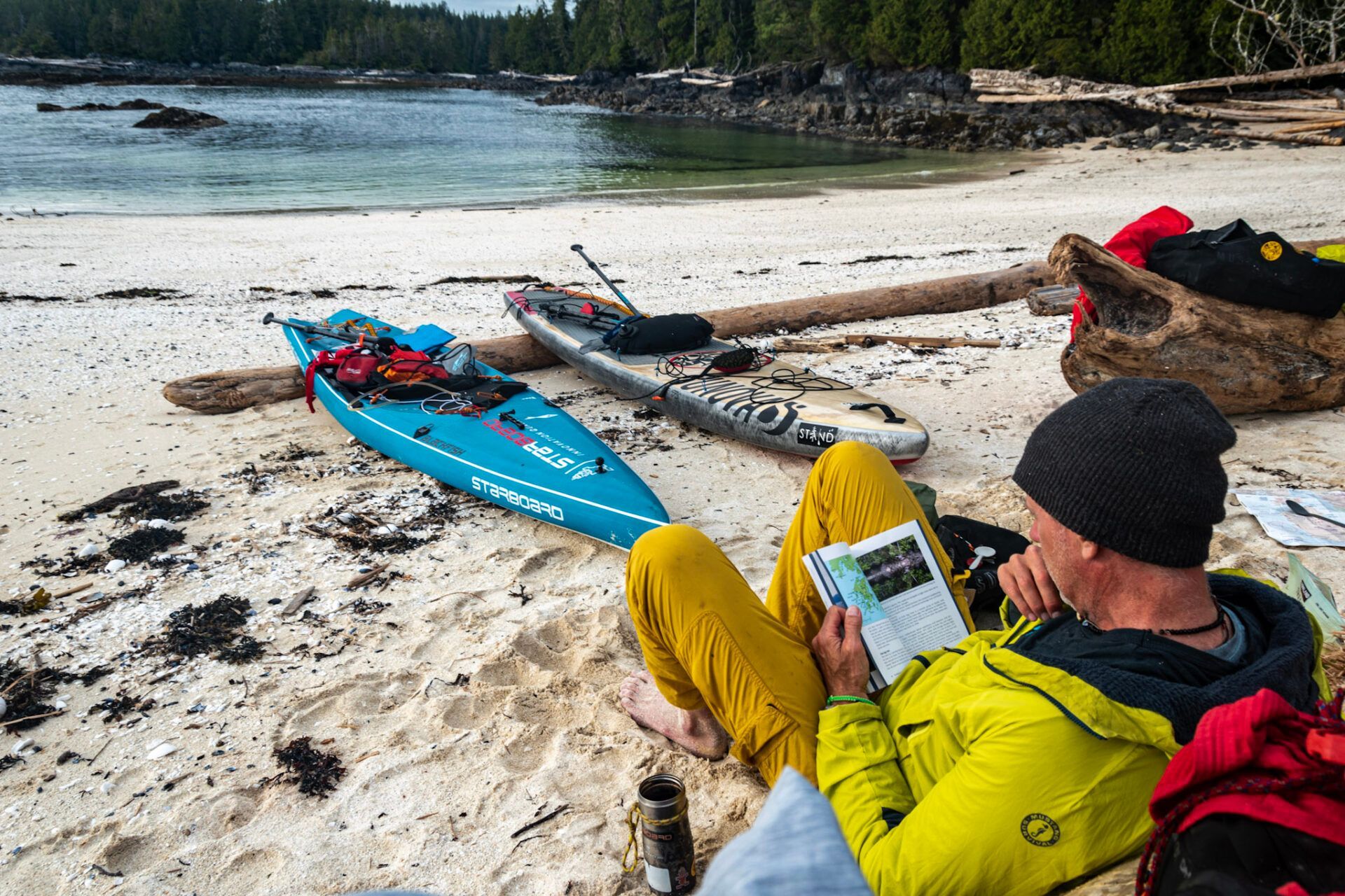 Kayaker in yellow jacket reading a map beside blue kayak on a sandy beach