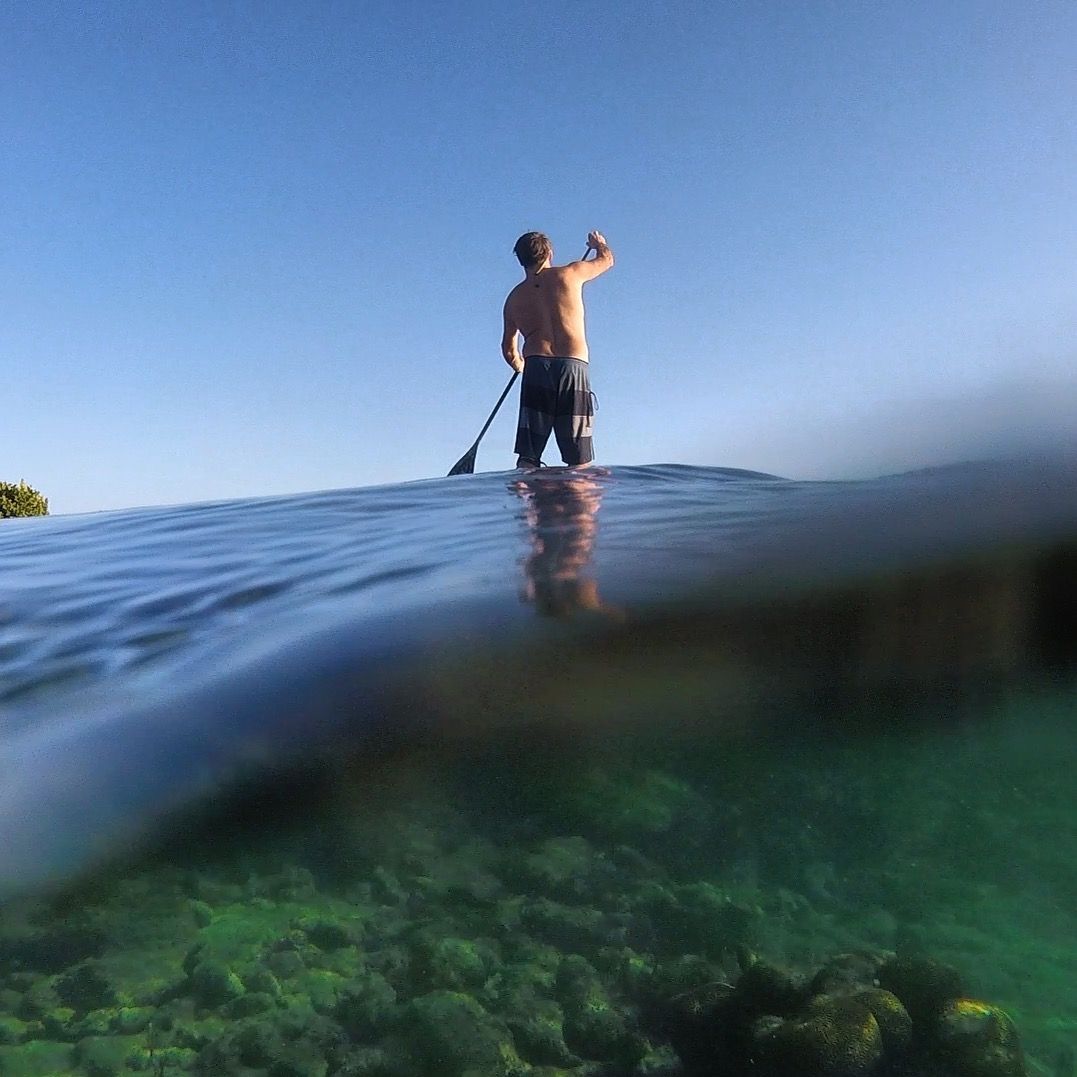 Person paddleboarding on calm water, viewed half above and half below the surface