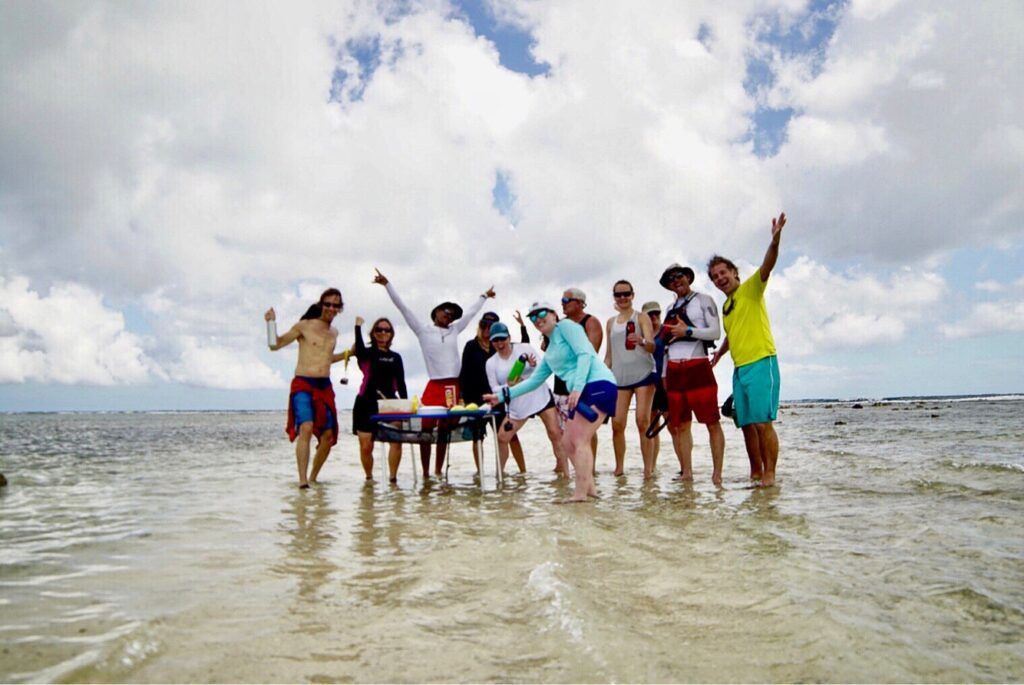 Group of people cheering and dancing in shallow beach water under a cloudy sky