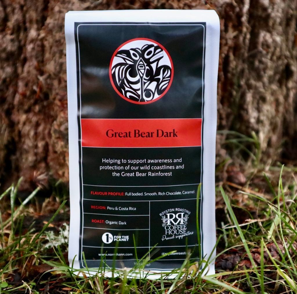 Black bag of Great Bear Dark coffee standing on grass in front of a tree.