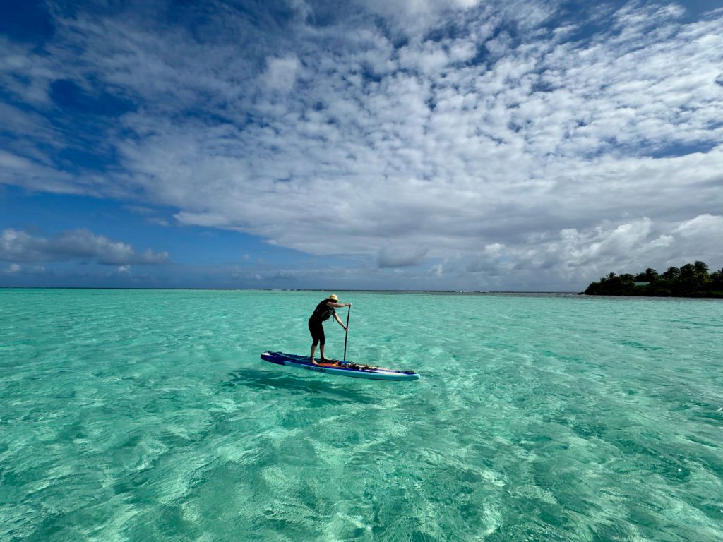 Person paddleboarding on clear turquoise water under a cloudy blue sky