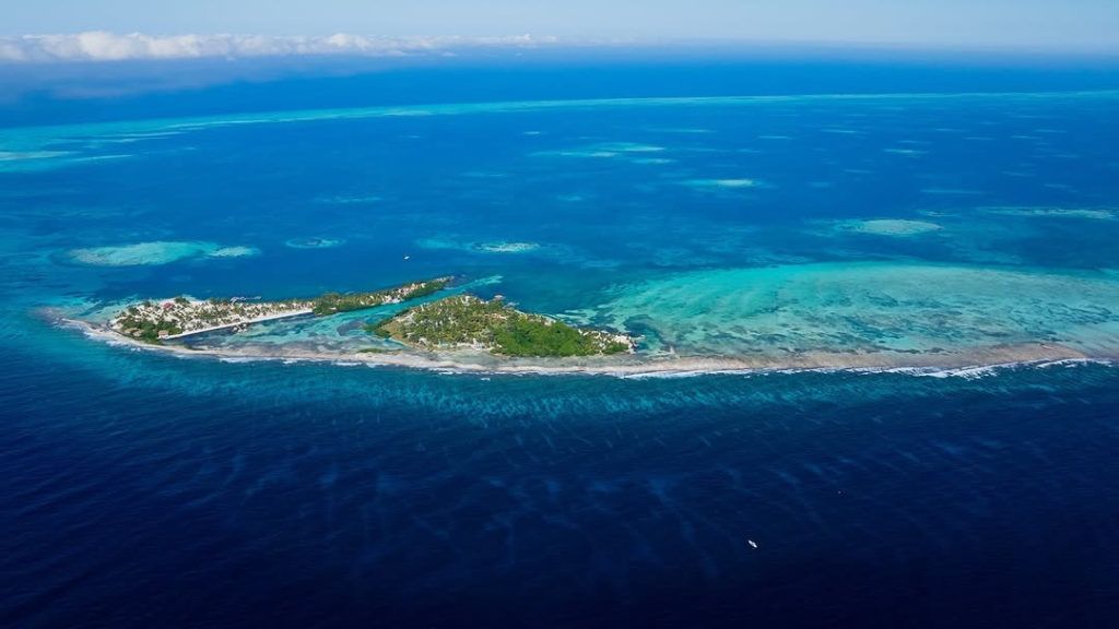 Aerial view of a small tropical island ringed by turquoise and deep blue ocean.