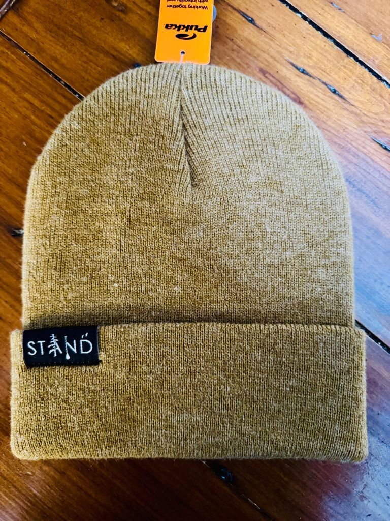 Olive knit beanie with folded cuff and black STAND label, displayed on a wooden surface.