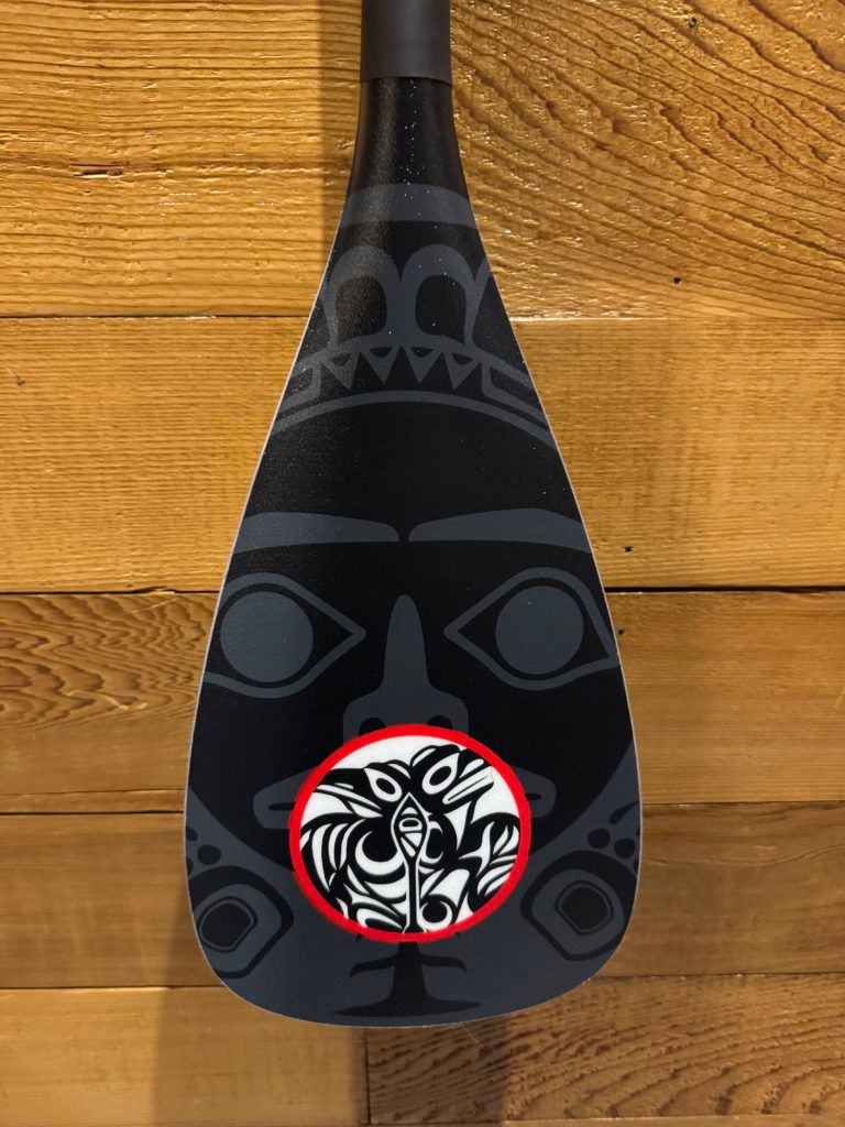 Black decorative vase with tribal patterns on a wooden background.