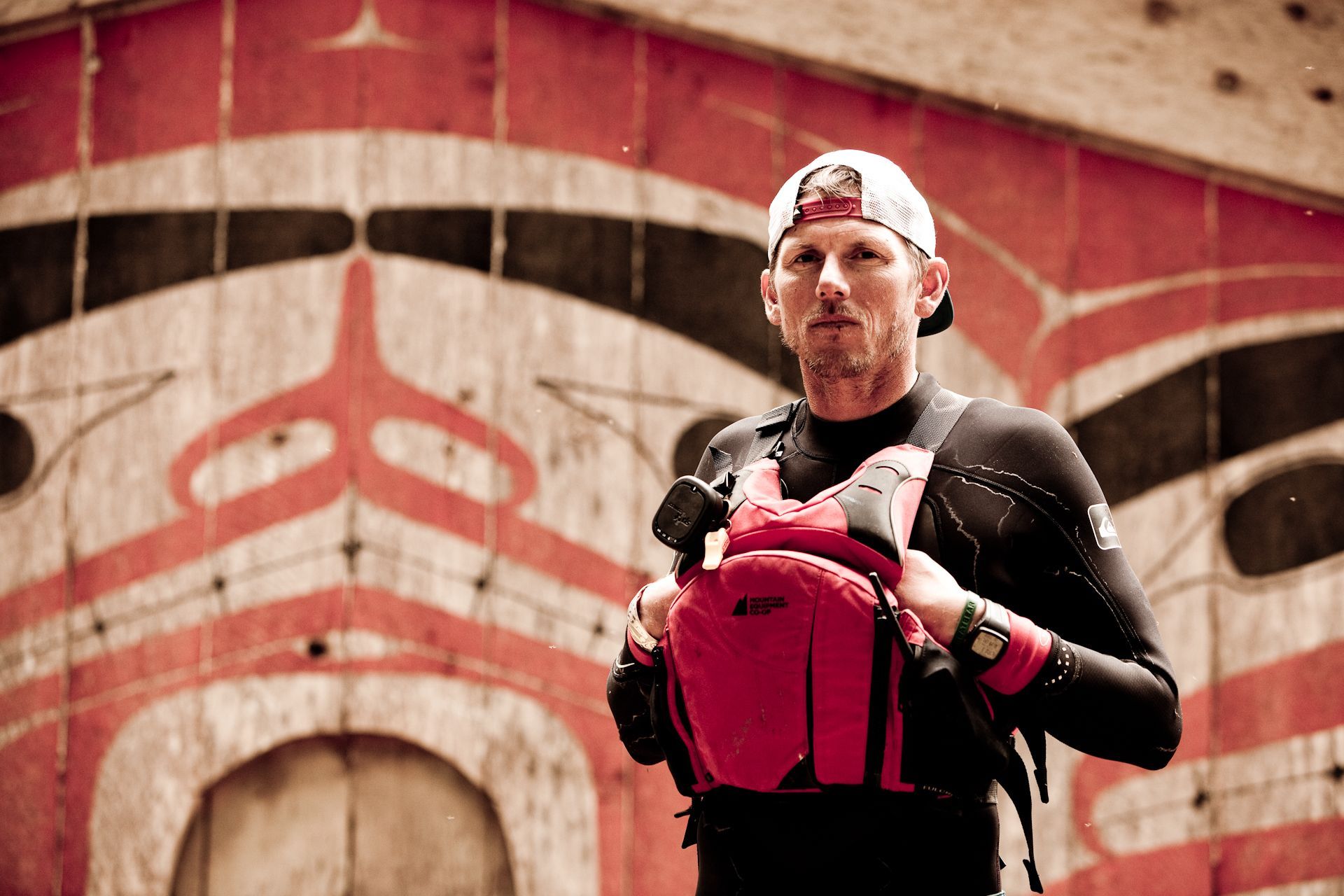 Athlete in red gear stands before a mural, wearing boxing gloves and a headband.