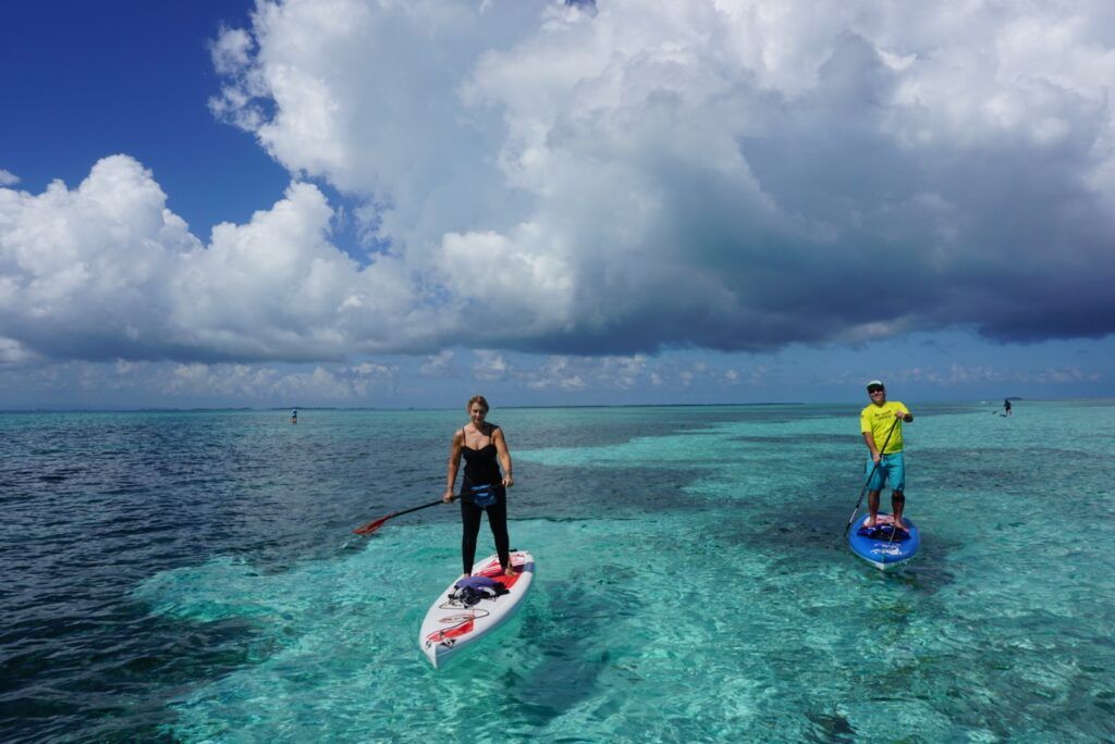Two people paddleboarding on clear turquoise water under dramatic clouds
