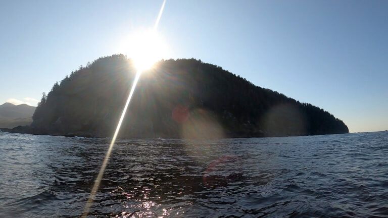 Sunlit island silhouette on a calm ocean at sunset with bright glare on the water