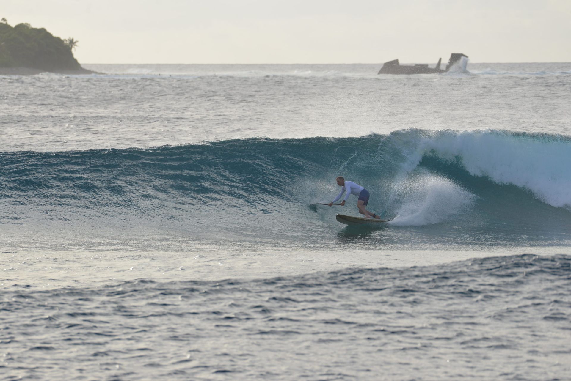 Surfer riding a wave at sunset with distant shoreline and boat in the background