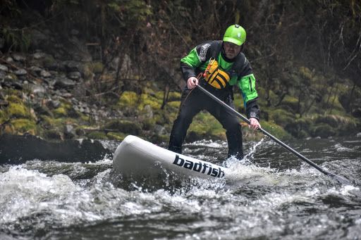 Paddler in a green helmet and black jacket steering a white kayak through rough river rapids