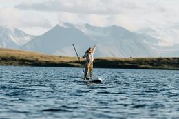 Person paddleboarding on a lake with mountains in the background