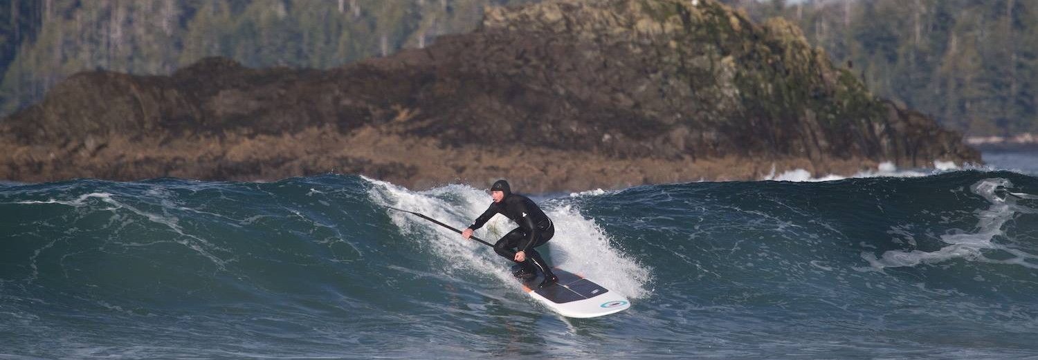 Person jet skiing on a wave with rocky coastline in the background