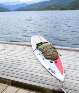 White kayak with gear on a wooden dock by a lake with mountains in the background