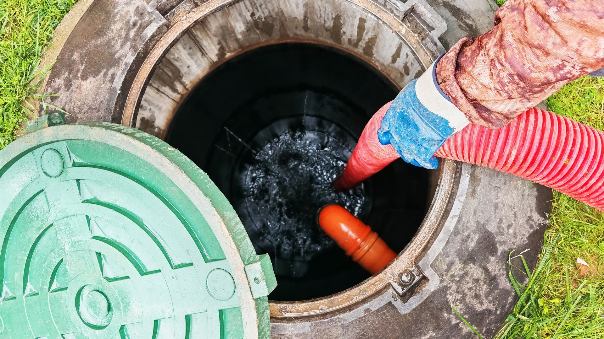 Worker pumping water from a manhole with red hose and green cover nearby