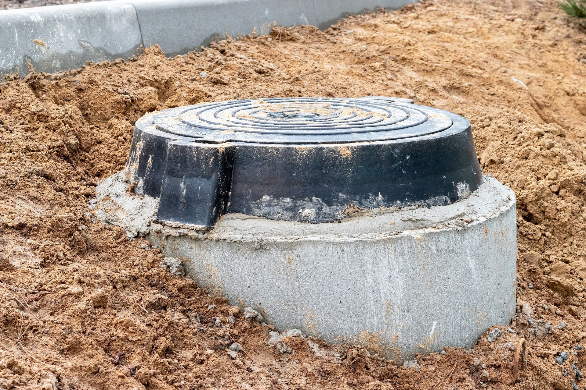 Concrete utility access cover protruding from dirt beside a curb