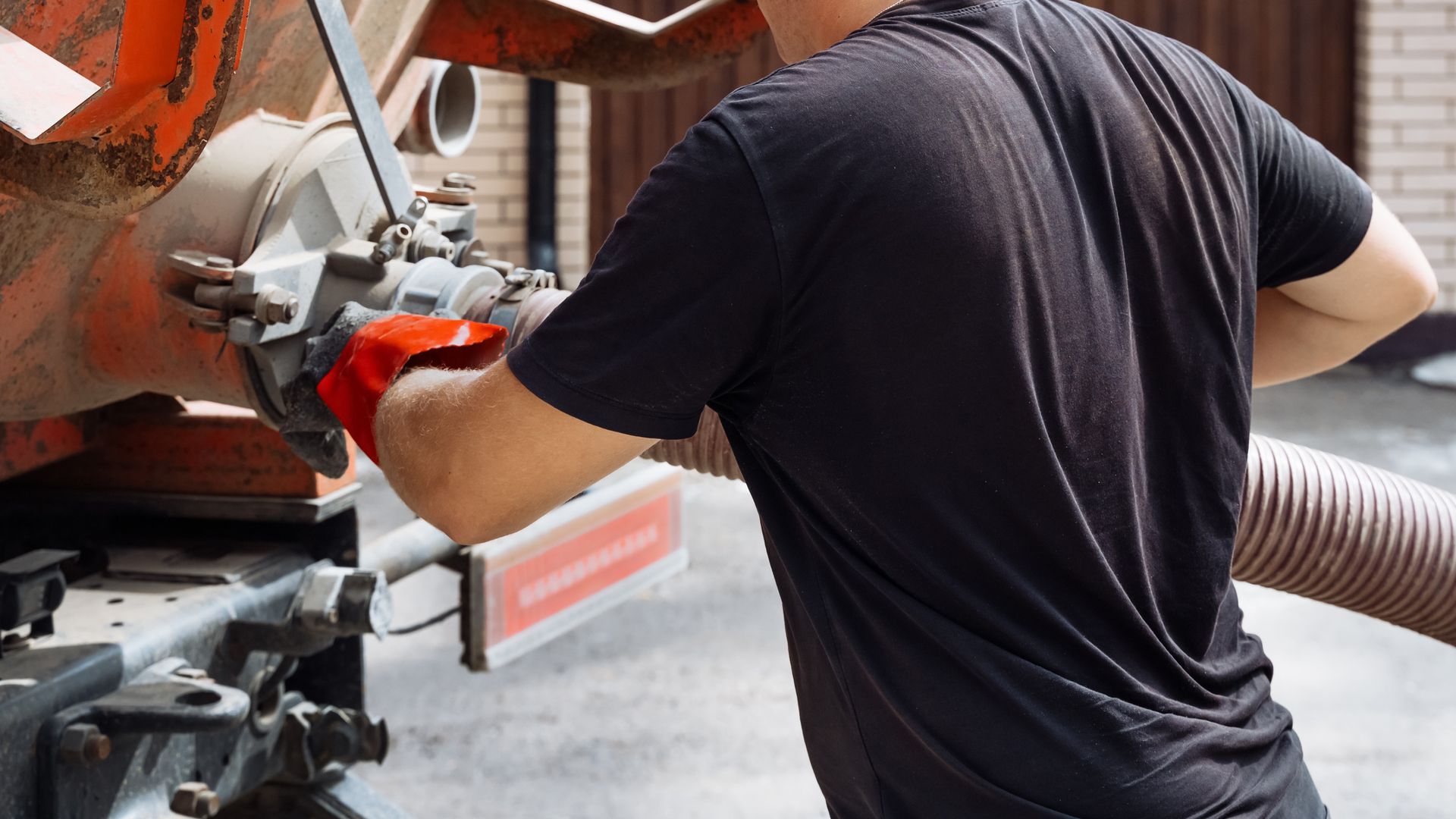 Worker in a black shirt handling equipment beside an orange machine on a construction site