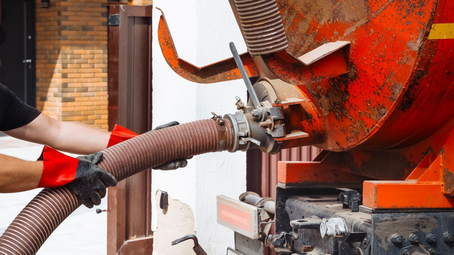 Worker cleaning a large orange cement mixer with a hose and brush