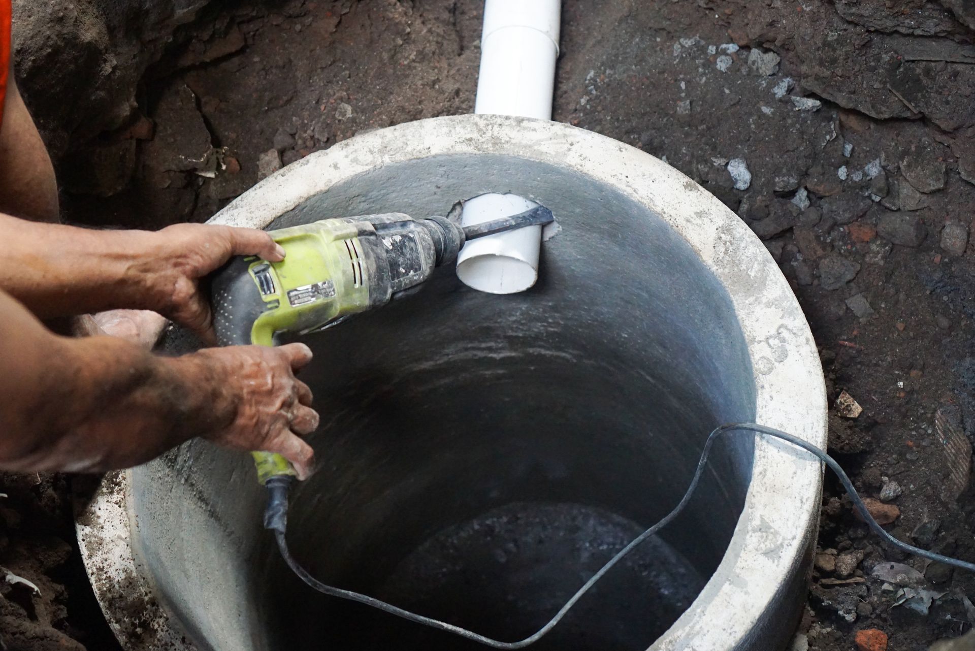 Hands holding a bottle over a concrete well, lowering a white cup with a wire.