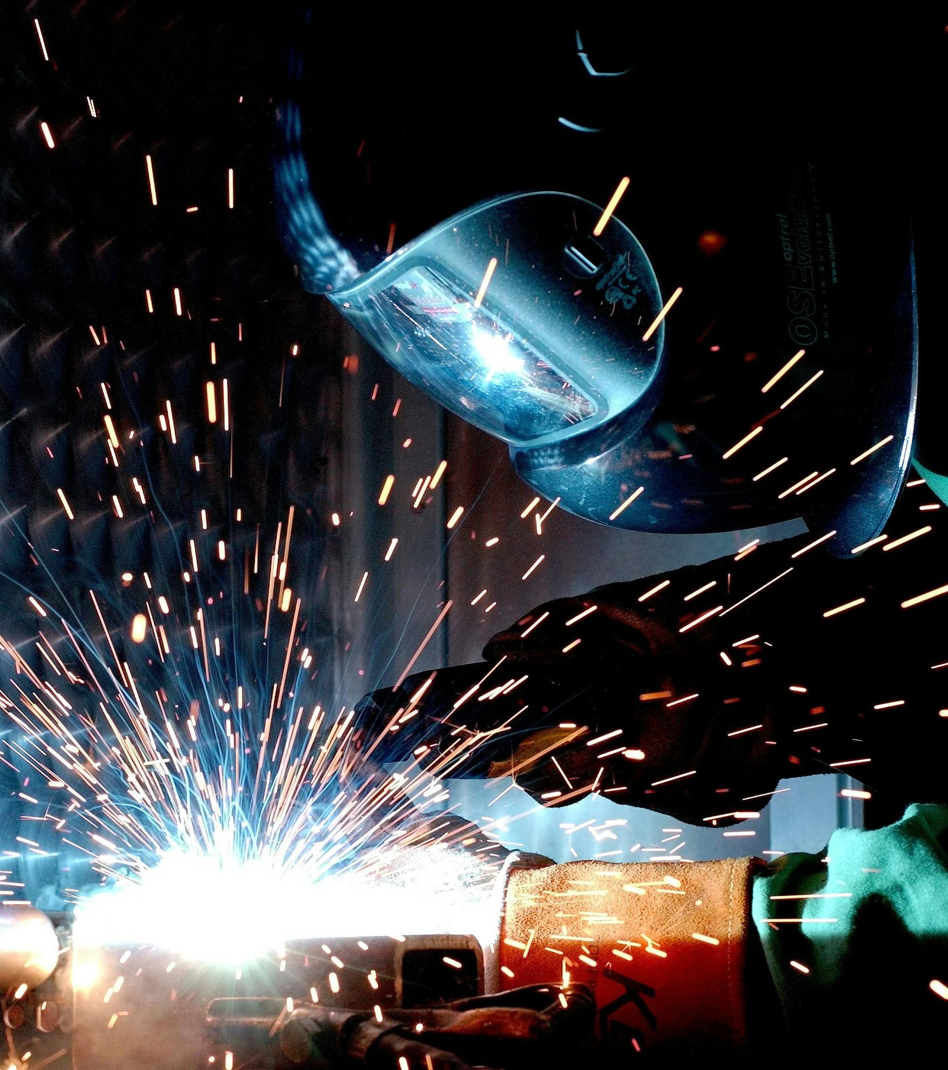 A man wearing a welding helmet is welding a piece of metal