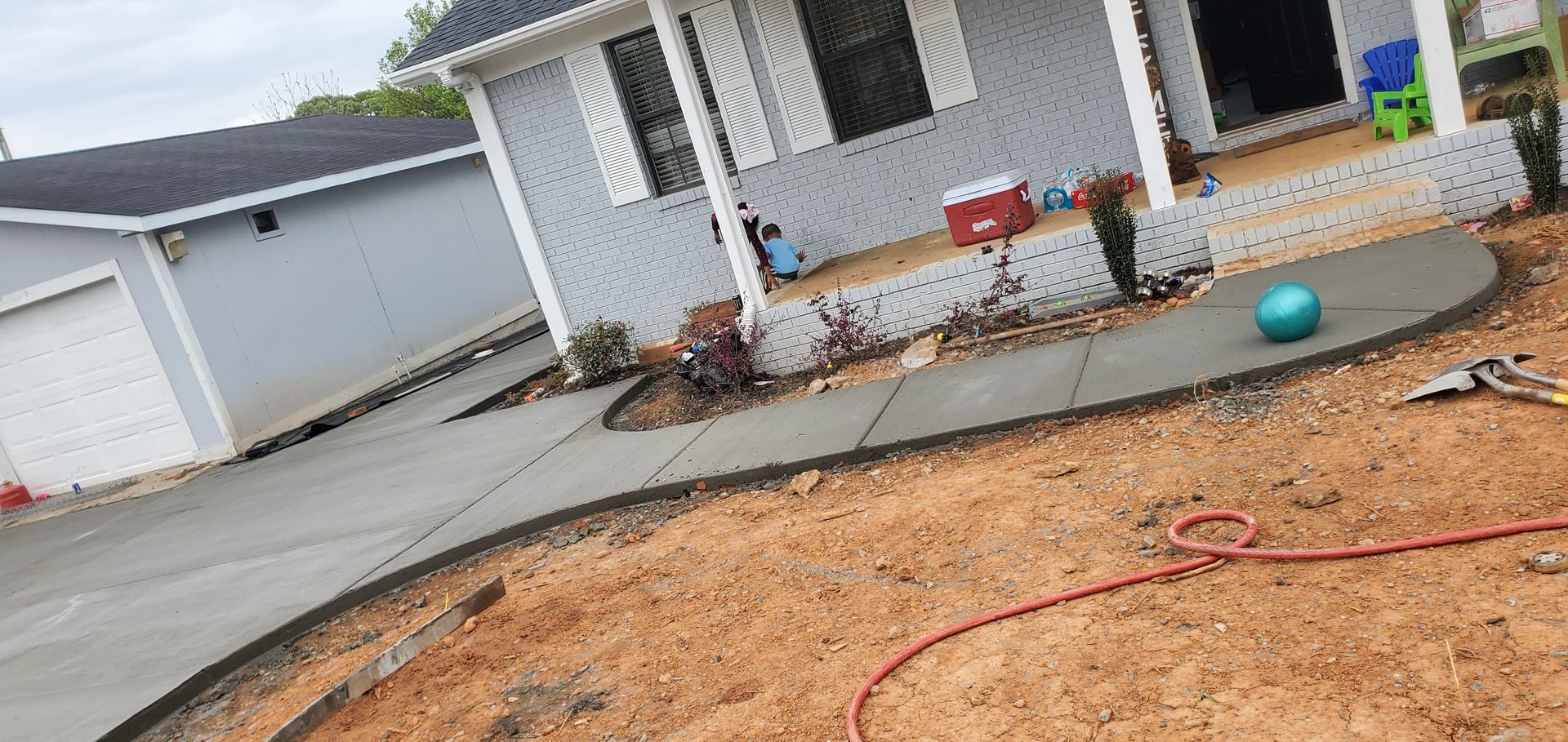 Front yard with bare dirt, red hose, porch, garage, and a blue ball near the house.