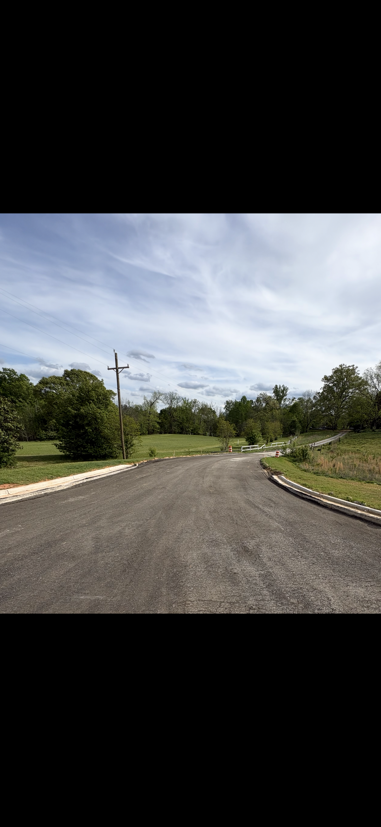 Gravel road curving through a green rural landscape under a partly cloudy sky