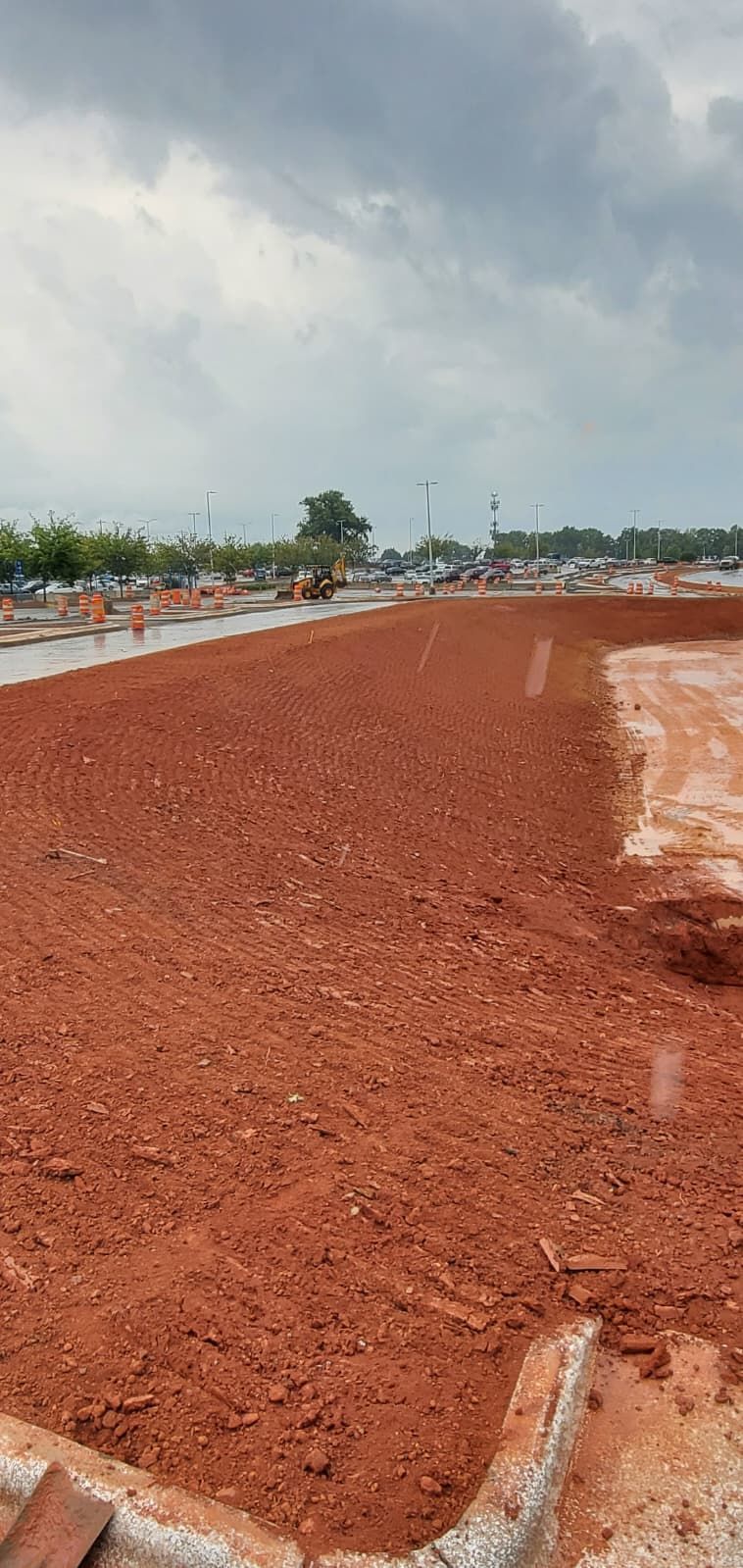 Red dirt construction site with a curving roadside under a cloudy sky.