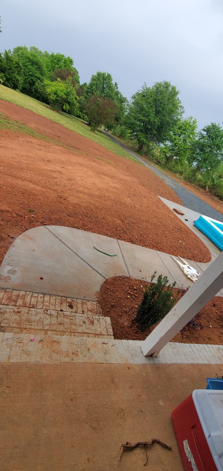 Diagonally tilted view of a muddy path, concrete steps, and green trees under an overcast sky