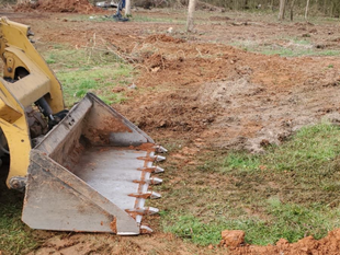 Yellow excavator bucket digging a dirt trench in a grassy field