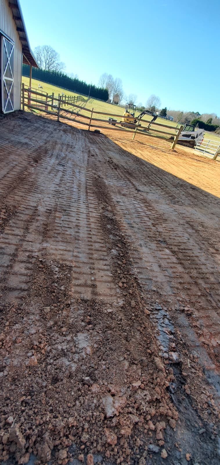 Rutted dirt driveway beside a wooden fence under a bright blue sky