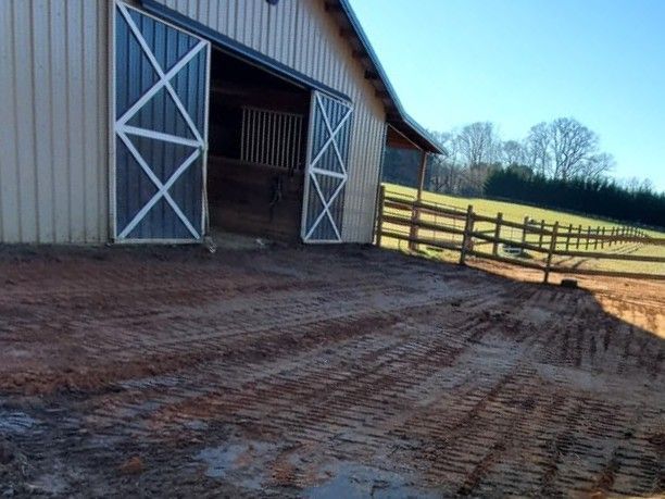 Barn with open white doors beside a muddy farmyard and wooden fence under a blue sky