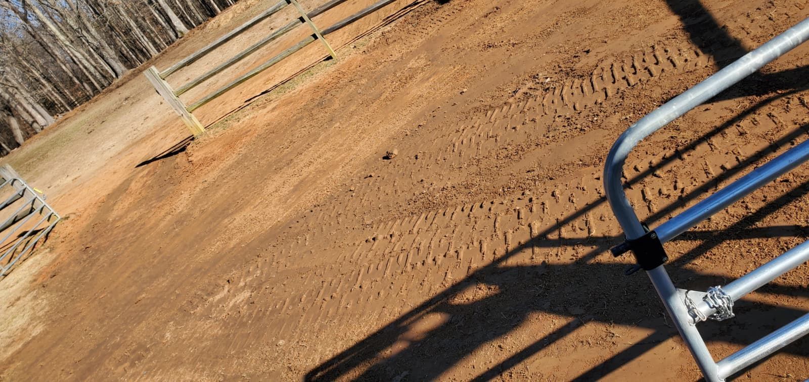 Dirt arena with a metal fence casting shadows on the ground