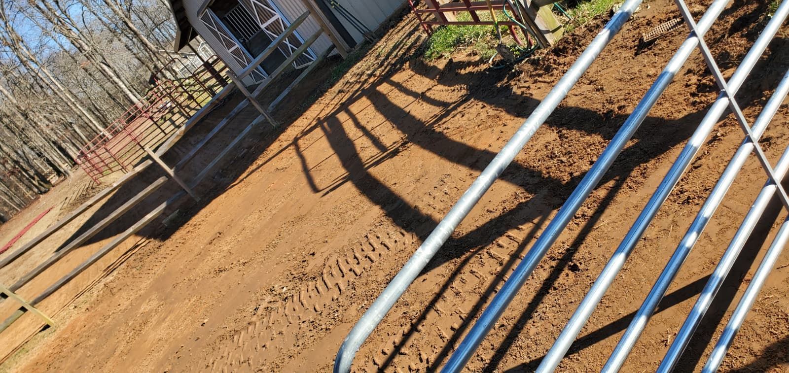 Sunlit dirt path beside a fence, with blue and white pipes lying diagonally in the foreground.
