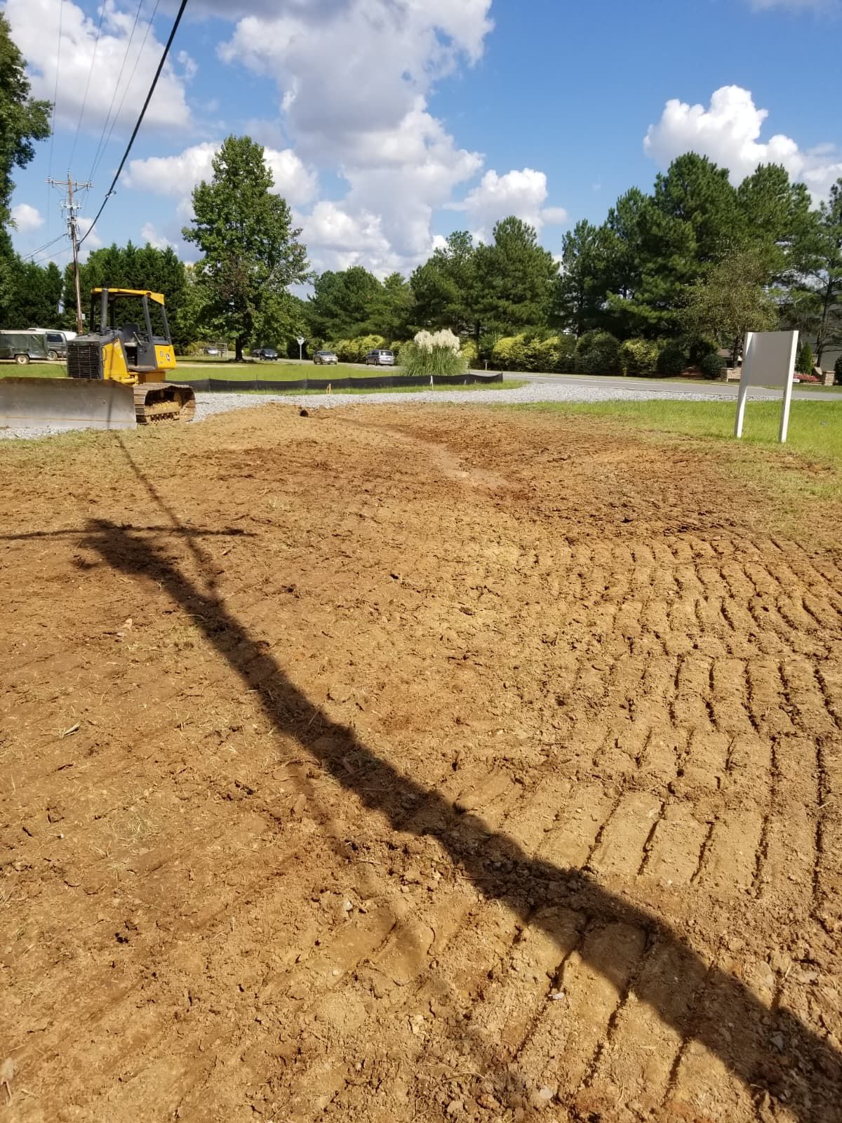 Construction site with freshly graded dirt, excavator at left, and a crane cable casting a shadow across the ground.