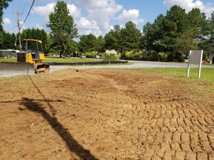 Construction site with dirt lot, small bulldozer, trees, and cloudy sky