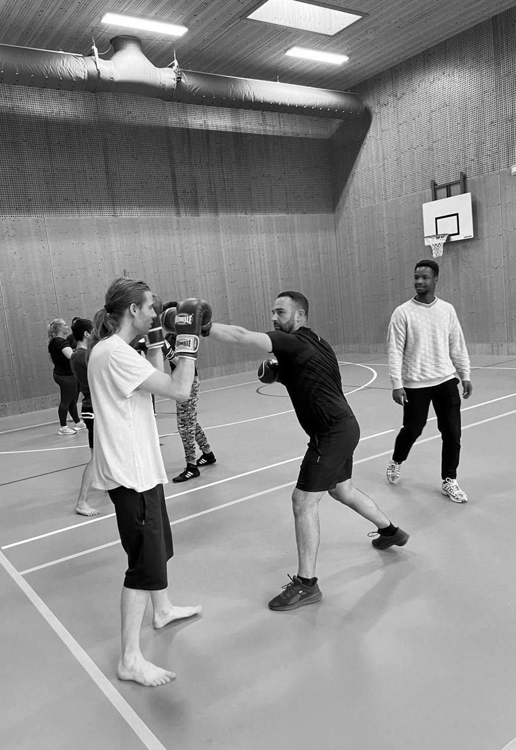 Mensen spelen basketbal in een sporthal, waarbij één van hen een speler verdedigt die de bal vlakbij het veld vasthoudt.