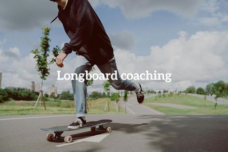 Een persoon in een donkere hoodie en spijkerbroek rijdt op een longboard over een geplaveid pad in een grasrijk park onder een blauwe hemel.