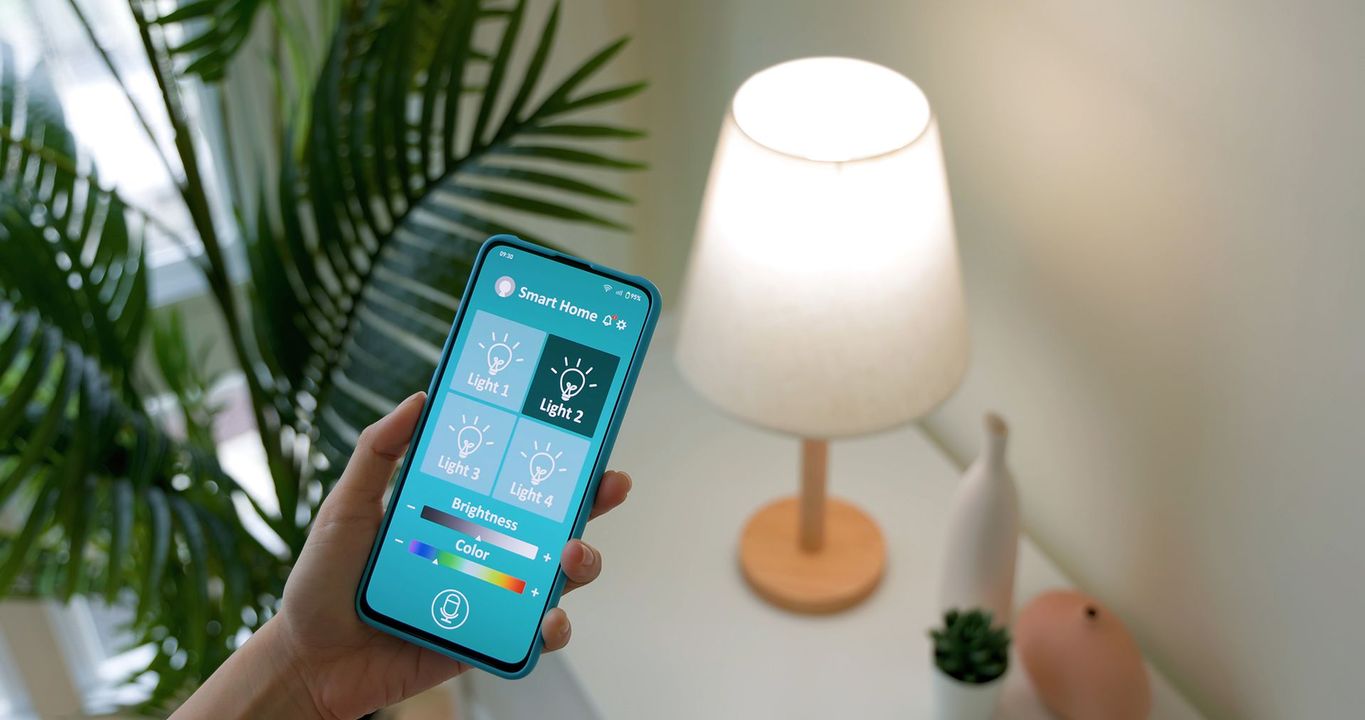 Telefono in mano che controlla una lampada intelligente; l'app mostra le opzioni di illuminazione.