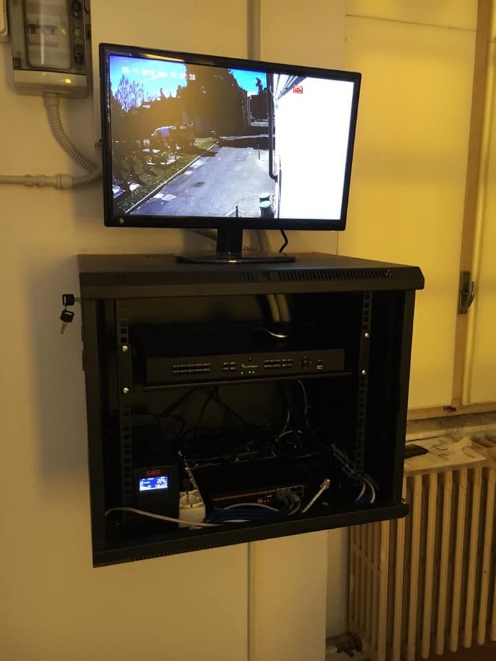 Sistema informatico nero montato su rack con monitor che mostra le riprese delle telecamere di sicurezza su una parete bianca.